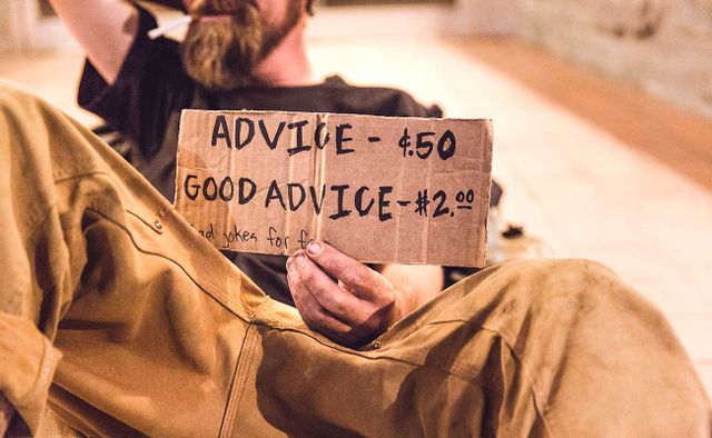 Homeless man holding hand written cardboard sign. Advice 50 cents. Good advice 2 dollars. Bad jokes for free.