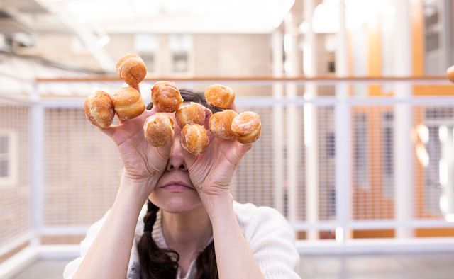 Women hiding face behind hands with a mini sugared doughnut stuck on the end of each finger and thumb.